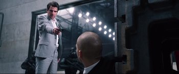 Movie still from “Hitman: Agent 47” (2015), directed by Aleksander Bach – A man in a suit and tie holding a gun in his hand; Medium shot, Over the shoulder angle