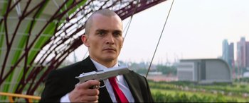 Movie still from “Hitman: Agent 47” (2015), directed by Aleksander Bach – A man in a suit and tie holding a gun in his hand; Close Up shot, Low angle