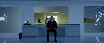 Movie still from “Hitman: Agent 47” (2015), directed by Aleksander Bach – A man in a suit and tie sitting in front of a desk; Wide shot, Low angle