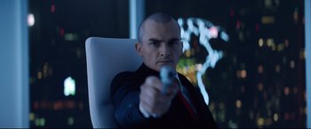 Movie still from “Hitman: Agent 47” (2015), directed by Aleksander Bach – A man in a suit and tie holding a gun in his hand; Medium shot, Low angle