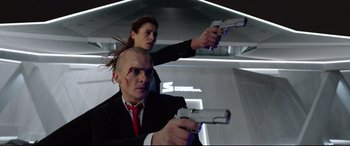 Movie still from “Hitman: Agent 47” (2015), directed by Aleksander Bach – A man and a woman holding guns while wearing suits; Medium shot, Low angle