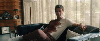 Movie still from “Gen V” (2023), created by Eric Kripke – A man sitting on a couch in front of a window; Medium shot, Low angle