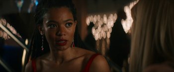 Movie still from “Gen V” (2023), created by Eric Kripke – A woman in a red dress and red earrings looking at the camera; Close Up shot, Over the shoulder angle
