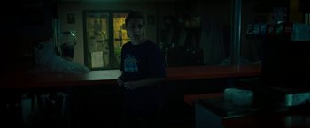 Movie still from “Gen V” (2023), created by Eric Kripke – A man standing in the dark holding a remote control; Medium shot, Over the shoulder angle