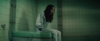 Movie still from “Gen V” (2023), created by Eric Kripke – A woman sitting on a bench chained to a metal chain; Medium shot, High angle