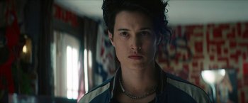 Movie still from “Gen V” (2023), created by Eric Kripke – A young man with long black hair wearing a blue jacket; Close Up shot, Low angle