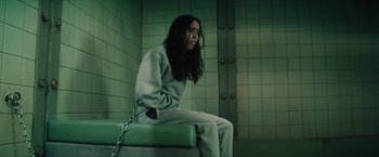 Movie still from “Gen V” (2023), created by Eric Kripke – A woman sitting on a bench chained to a metal chain; Medium shot, Low angle