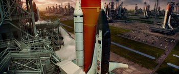 Movie still from “Geostorm” (2017), directed by Dean Devlin – Three rockets are parked in a field near a factory; Extreme Wide shot, Overhead angle