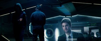 Movie still from “Geostorm” (2017), directed by Dean Devlin – A man standing in front of an image of a man in a suit; Medium shot, Over the shoulder angle