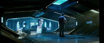 Movie still from “Geostorm” (2017), directed by Dean Devlin – A man standing in front of an image of a man; Wide shot, Over the shoulder angle