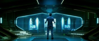 Movie still from “Geostorm” (2017), directed by Dean Devlin – A man standing in front of a room with two monitors; Wide shot, Low angle