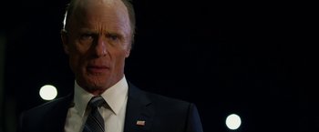 Movie still from “Geostorm” (2017), directed by Dean Devlin – A man in a suit and tie standing in front of a black background; Close Up shot, Low angle