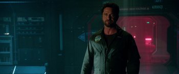 Movie still from “Geostorm” (2017), directed by Dean Devlin – A man standing in front of a wall in a dark room; Medium shot, Over the shoulder angle