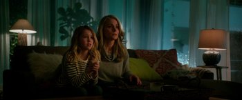 Movie still from “Geostorm” (2017), directed by Dean Devlin – A woman sitting next to a young girl on a couch; Medium shot, Low angle