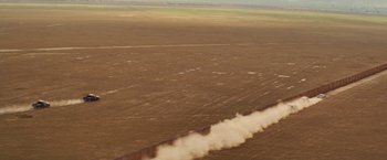 Movie still from “Get the Gringo” (2012), directed by Adrian Grunberg – An aerial view of an open field with smoke billowing out of it; Extreme Wide shot, Low angle