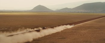 Movie still from “Get the Gringo” (2012), directed by Adrian Grunberg – A truck driving down a dirt road near mountains; Extreme Wide shot, High angle