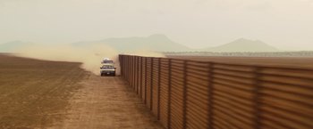 Movie still from “Get the Gringo” (2012), directed by Adrian Grunberg – A police car driving down a dirt road next to a wall; Extreme Wide shot, Low angle
