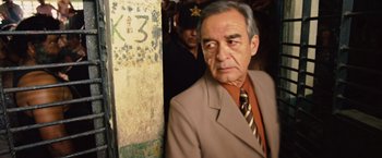 Movie still from “Get the Gringo” (2012), directed by Adrian Grunberg – An older man wearing a suit and tie standing in front of a wall; Close Up shot, Over the shoulder angle