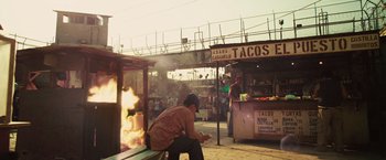 Movie still from “Get the Gringo” (2012), directed by Adrian Grunberg – A man sitting on a bench in front of an open fire; Wide shot, High angle