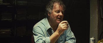 Movie still from “Get the Gringo” (2012), directed by Adrian Grunberg – An older man sitting down with a cup in his hand; Close Up shot, Low angle