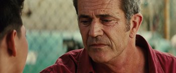 Movie still from “Get the Gringo” (2012), directed by Adrian Grunberg – An older man with a red shirt is looking at the camera; Close Up shot, Over the shoulder angle