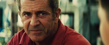 Movie still from “Get the Gringo” (2012), directed by Adrian Grunberg – An older man wearing a red shirt looking at the camera; Close Up shot, Over the shoulder angle