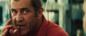 Movie still from “Get the Gringo” (2012), directed by Adrian Grunberg – An older man wearing a red shirt looking into the distance; Close Up shot, Over the shoulder angle