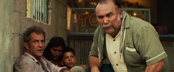 Movie still from “Get the Gringo” (2012), directed by Adrian Grunberg – An older man with a beard and a woman and a child; Medium shot, Low angle