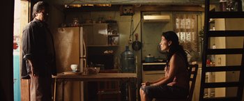 Movie still from “Get the Gringo” (2012), directed by Adrian Grunberg – A woman sitting on a chair in a kitchen; Medium shot, Over the shoulder angle