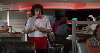 Movie still from “Ghost World” (2001), directed by Terry Zwigoff – A man with curly hair and a red bow tie is writing on a notepad; Medium shot, Over the shoulder angle