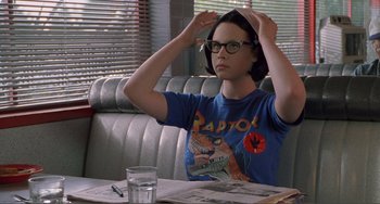 Movie still from “Ghost World” (2001), directed by Terry Zwigoff – A person sitting at a table in front of a glass of water; Medium shot, Over the shoulder angle