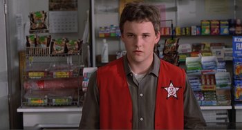 Movie still from “Ghost World” (2001), directed by Terry Zwigoff – A young man in a red vest standing in a store; Close Up shot, Over the shoulder angle