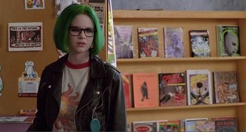 Movie still from “Ghost World” (2001), directed by Terry Zwigoff – A woman with green hair standing in front of a book shelf; Medium shot, Over the shoulder angle