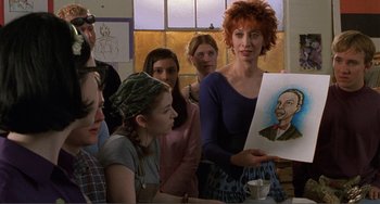 Movie still from “Ghost World” (2001), directed by Terry Zwigoff – A group of people gathered around a woman holding up a picture; Close Up shot, Over the shoulder angle