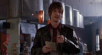 Movie still from “Ghost World” (2001), directed by Terry Zwigoff – A man in a leather jacket holding a pen and paper; Medium shot, Over the shoulder angle