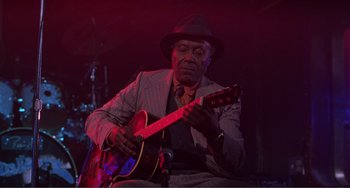Movie still from “Ghost World” (2001), directed by Terry Zwigoff – An older man in a hat playing a guitar; Medium shot, Low angle
