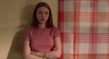 Movie still from “Ghost World” (2001), directed by Terry Zwigoff – A woman in a pink shirt is standing in front of a red and white checkered curtain; Medium shot, Low angle