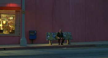 Movie still from “Ghost World” (2001), directed by Terry Zwigoff – A man sitting on top of a bench on a sidewalk; Extreme Wide shot, Low angle