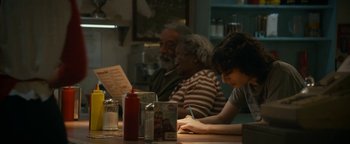 Movie still from “Ghostbusters: Afterlife” (2021), directed by Jason Reitman – A group of people sitting at a table in a restaurant; Medium shot, Over the shoulder angle