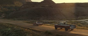 Movie still from “Ghostbusters: Afterlife” (2021), directed by Jason Reitman – A group of cars driving down a dirt road near a hill; Extreme Wide shot, High angle