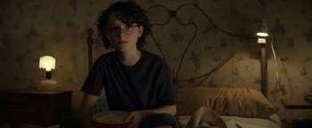 Movie still from “Ghostbusters: Afterlife” (2021), directed by Jason Reitman – A woman sitting on a bed with a bowl of food; Medium shot, High angle