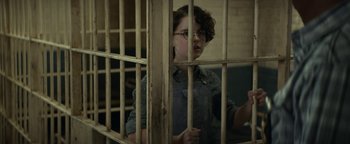 Movie still from “Ghostbusters: Afterlife” (2021), directed by Jason Reitman – A person standing behind bars in a jail cell; Medium shot, High angle