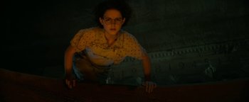 Movie still from “Ghostbusters: Afterlife” (2021), directed by Jason Reitman – A woman in a yellow shirt is standing in a dark room; Medium shot, Low angle