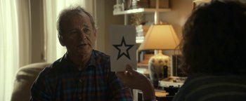 Movie still from “Ghostbusters: Afterlife” (2021), directed by Jason Reitman – An older man holding up a paper with a star on it; Close Up shot, Over the shoulder angle