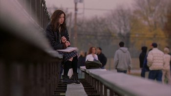 A woman sitting on a railing while holding a book