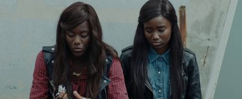 Movie still from “Girlhood” (2014), directed by Céline Sciamma – Two young women sitting next to each other in front of a wall; Close Up shot, High angle