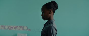 Movie still from “Girlhood” (2014), directed by Céline Sciamma – A young woman with braids standing in front of a blue wall; Close Up shot, Over the shoulder angle