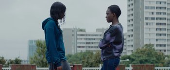 Movie still from “Girlhood” (2014), directed by Céline Sciamma – Two young women standing next to each other in front of a building; Medium shot, Over the shoulder angle