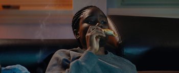 Movie still from “Girlhood” (2014), directed by Céline Sciamma – A young girl eating a hot dog on a bun while sitting in a chair; Medium shot, High angle