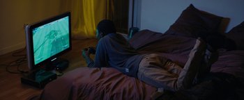 Movie still from “Girlhood” (2014), directed by Céline Sciamma – A man laying on a bed playing a video game; Wide shot, High angle
